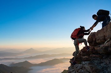 A hiker helping another hiker to the top of a mountain