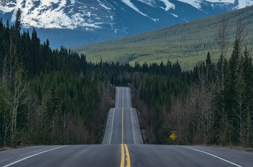 Looking down tree-lined two-lane highway with mountains in the distance