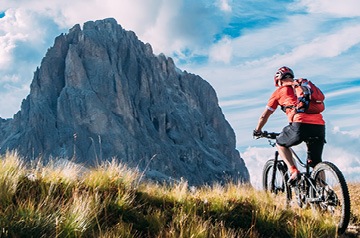 Mountain biker on a trail with a rocky mountain in the background.