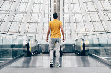 Person in light-filled glass-domed area contemplating which escalator to take
