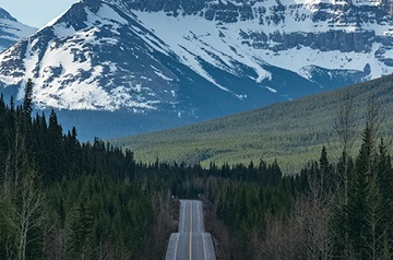 View of two-lane road cutting through forest heading towards mountains