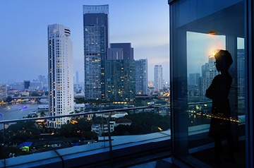 Businessperson looking out office window onto cityscape at dusk