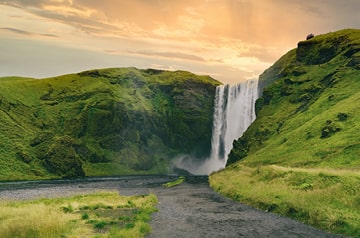 Waterfall between green mountains at dawn