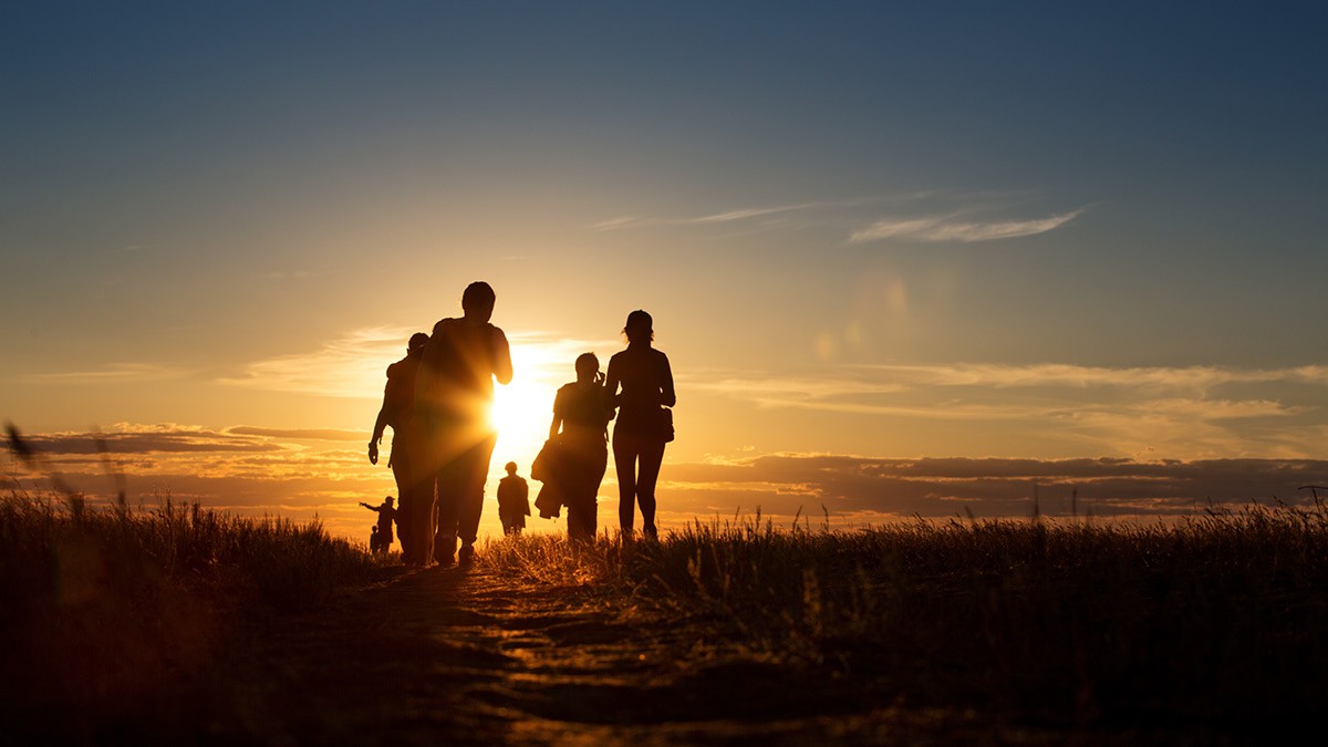 Group of people walking on a trail silhouetted in the setting sun.