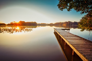 Looking along dock and across quiet lake at sunrise