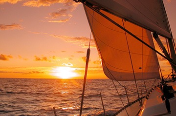 Sunset seen from a sailboat, with a full sail in the foreground