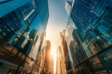 Looking skyward through alley of glass paneled skyscrapers towards the rising sun