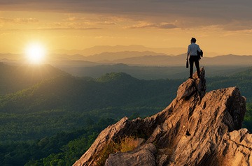 Climber on a rocky summit facing a sunset